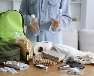 Photo of Survival kit. Woman packing different emergency supplies at wooden table indoors, closeup