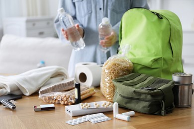 Photo of Survival kit. Woman packing different emergency supplies at wooden table indoors, selective focus