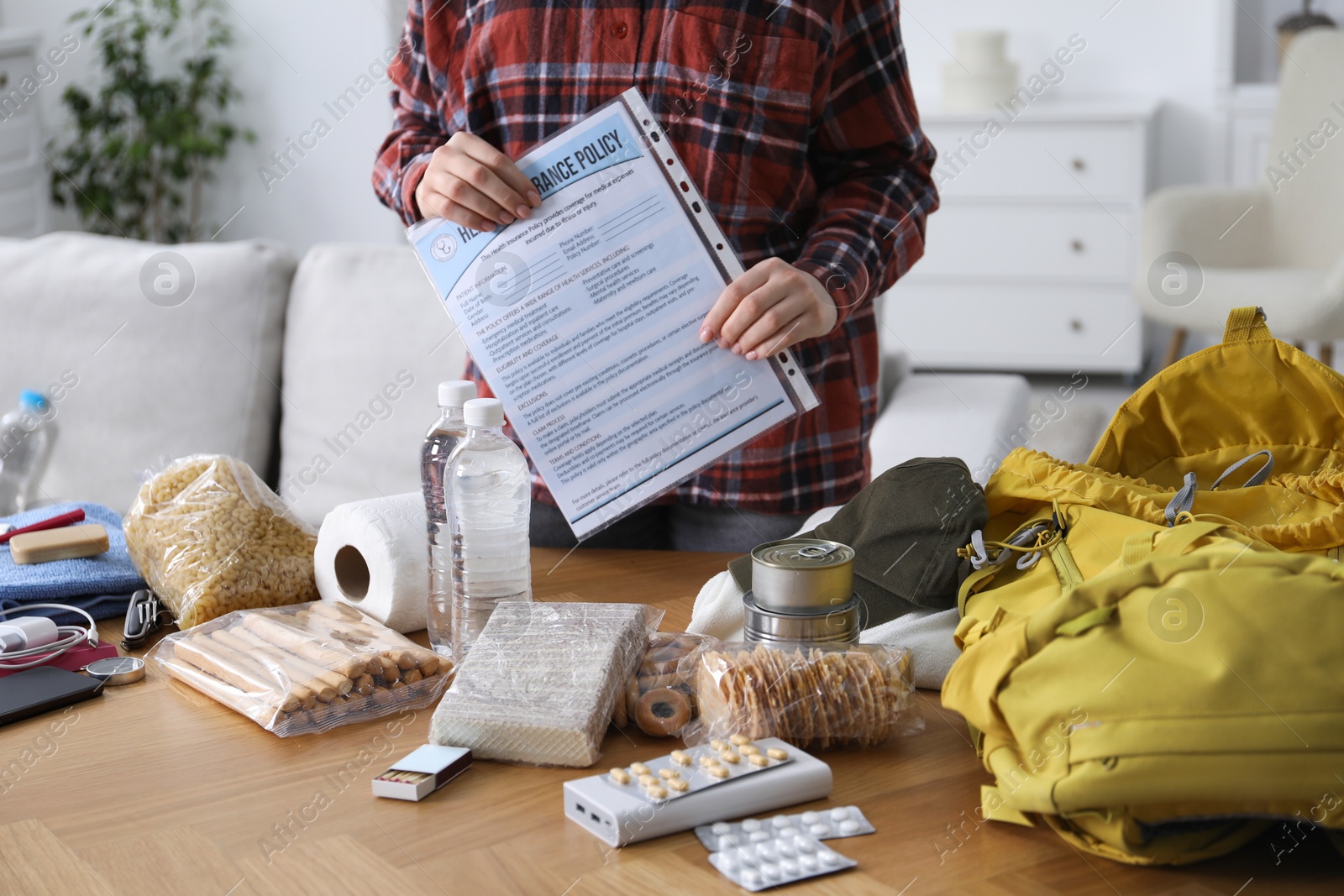 Survival kit. Woman holding documents near table with different emergency supplies indoors, closeup Photo of Survival kit. Woman holding documents near table with different emergency supplies indoors, closeup