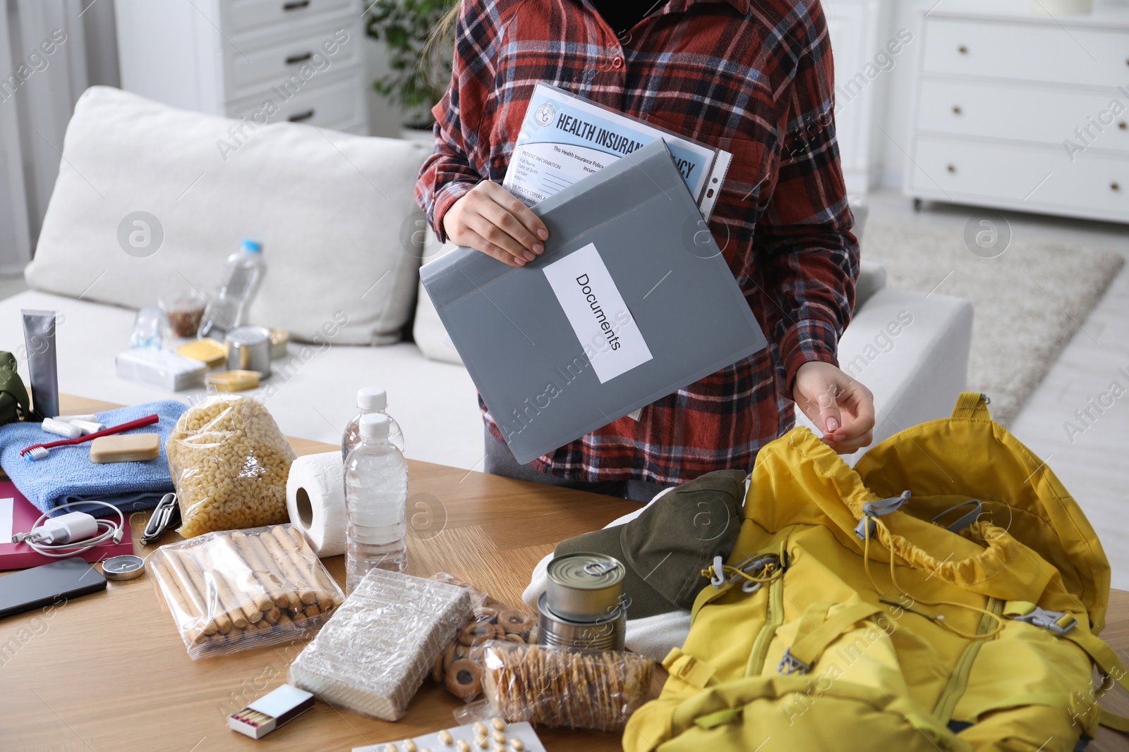Survival kit. Woman holding documents near table with different emergency supplies indoors, closeup Photo of Survival kit. Woman holding documents near table with different emergency supplies indoors, closeup