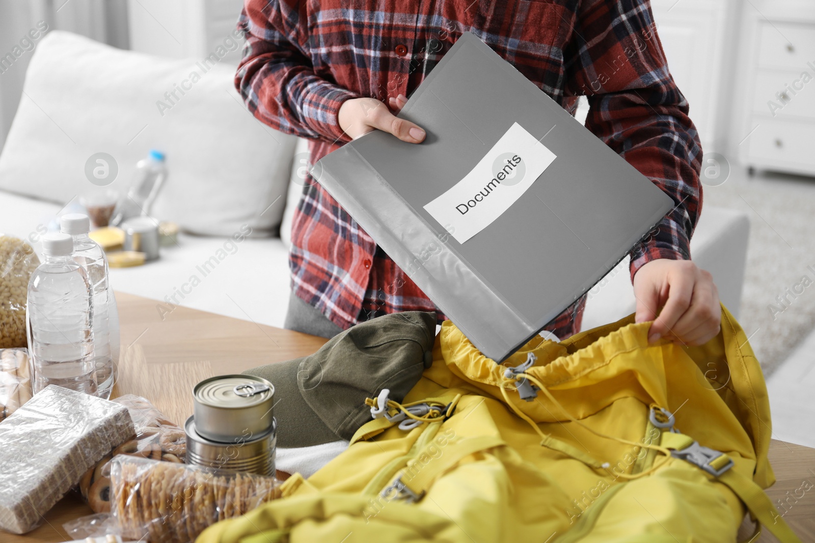 Survival kit. Woman putting documents into backpack at table indoors, closeup Photo of Survival kit. Woman putting documents into backpack at table indoors, closeup