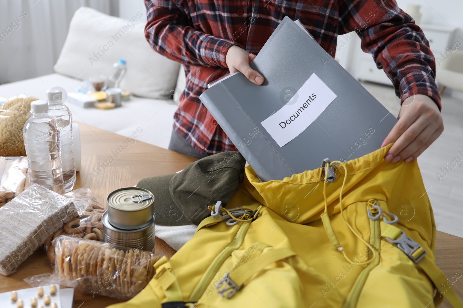 Survival kit. Woman putting documents into backpack at table indoors, closeup Photo of Survival kit. Woman putting documents into backpack at table indoors, closeup