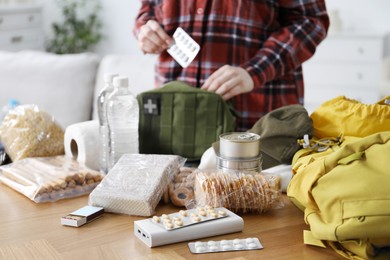Photo of Survival kit. Woman putting medicine into bag at wooden table indoors, closeup