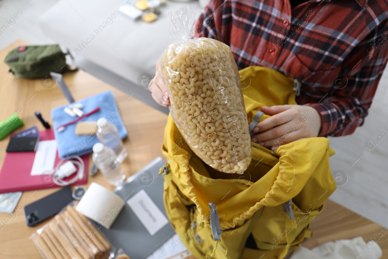Survival kit. Woman putting raw pasta into backpack at table indoors, above view Photo of Survival kit. Woman putting raw pasta into backpack at table indoors, above view