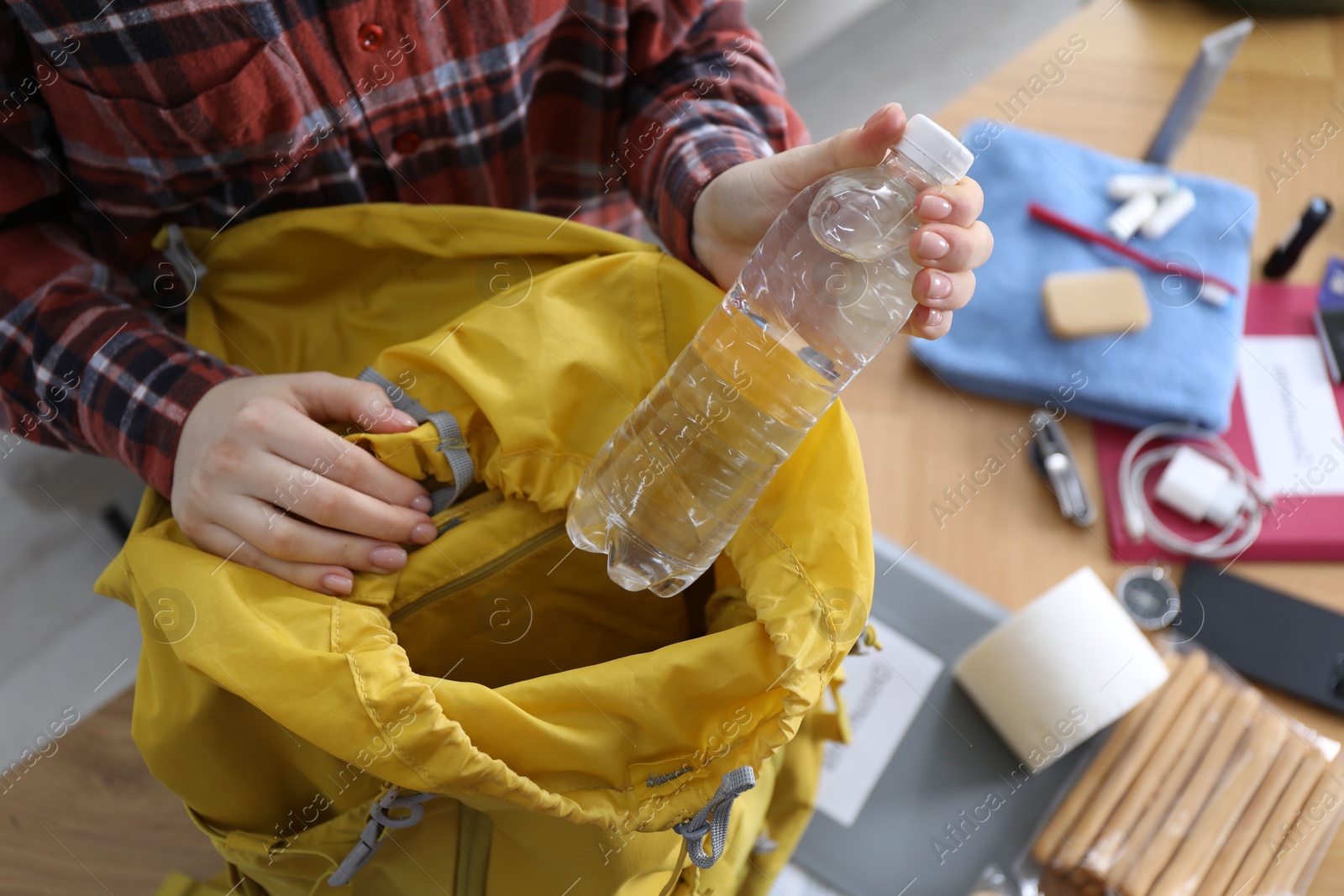 Survival kit. Woman putting bottle of water into backpack at table indoors, above view Photo of Survival kit. Woman putting bottle of water into backpack at table indoors, above view