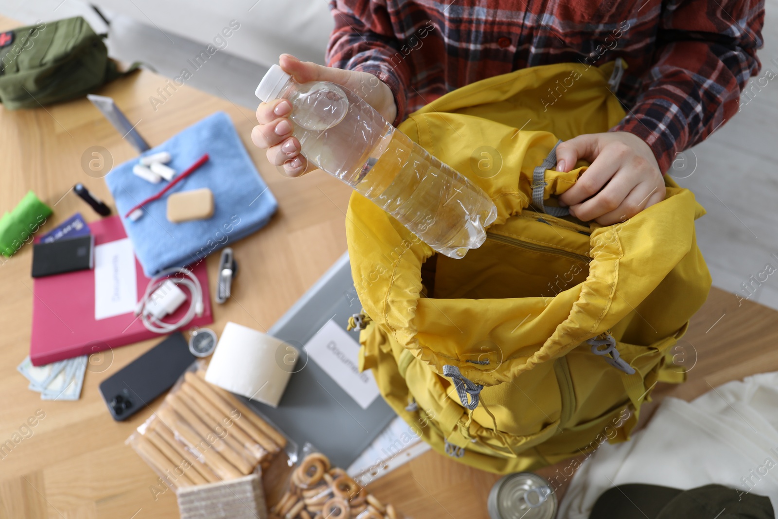 Survival kit. Woman putting bottle of water into backpack at wooden table indoors, above view Photo of Survival kit. Woman putting bottle of water into backpack at wooden table indoors, above view