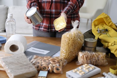 Photo of Survival kit. Woman packing different emergency supplies at wooden table indoors, closeup