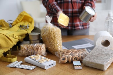 Photo of Survival kit. Woman packing different emergency supplies at wooden table indoors, selective focus