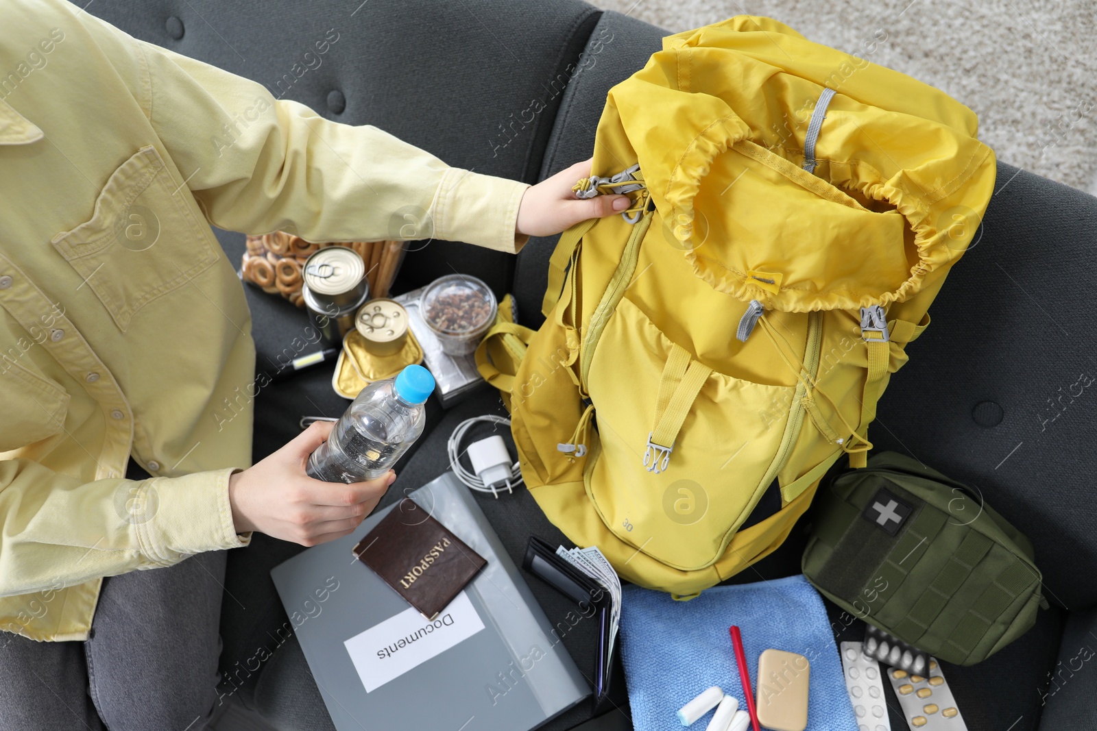 Survival kit. Woman putting bottle of water into backpack on sofa indoors, above view Photo of Survival kit. Woman putting bottle of water into backpack on sofa indoors, above view