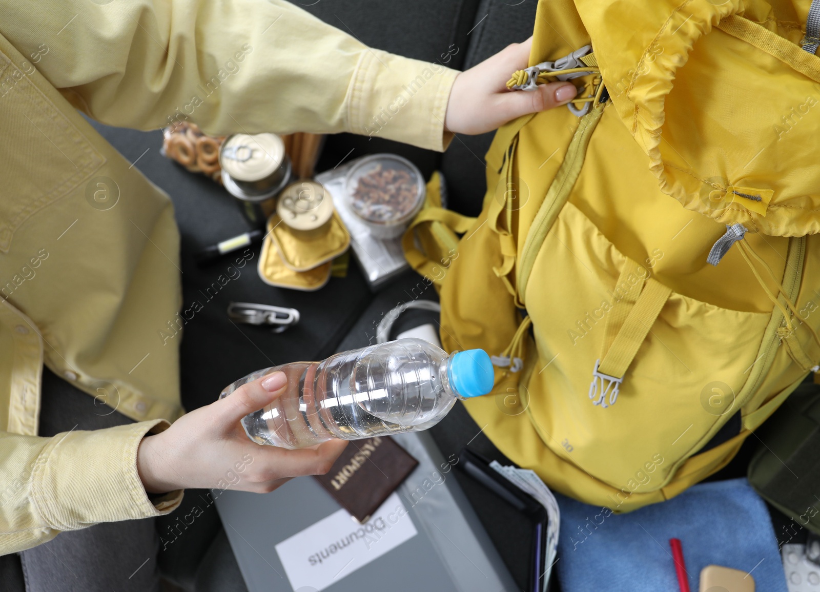 Survival kit. Woman putting bottle of water into backpack on sofa indoors, above view Photo of Survival kit. Woman putting bottle of water into backpack on sofa indoors, above view