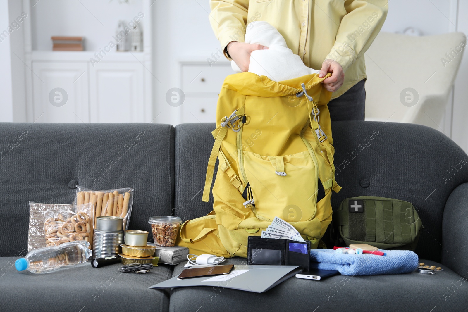 Survival kit. Woman putting clothes into backpack indoors, closeup Photo of Survival kit. Woman putting clothes into backpack indoors, closeup