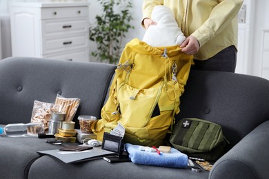Photo of Survival kit. Woman putting clothes into backpack indoors, closeup