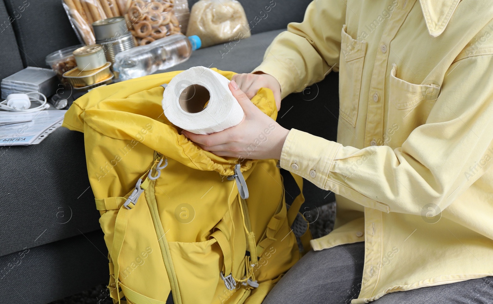 Survival kit. Woman putting toilet paper roll into backpack on floor indoors, closeup Photo of Survival kit. Woman putting toilet paper roll into backpack on floor indoors, closeup