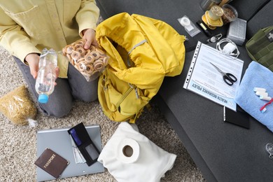 Photo of Survival kit. Woman packing different emergency supplies on floor indoors, above view