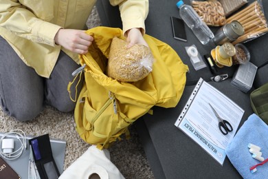 Photo of Survival kit. Woman putting raw pasta into backpack indoors, above view