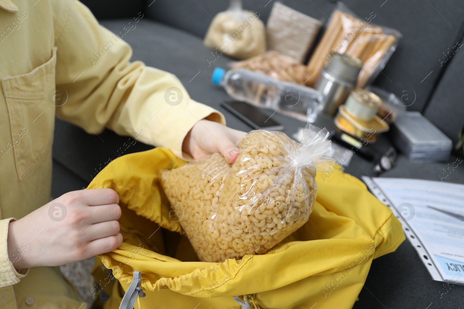 Survival kit. Woman putting raw pasta into backpack indoors, closeup Photo of Survival kit. Woman putting raw pasta into backpack indoors, closeup