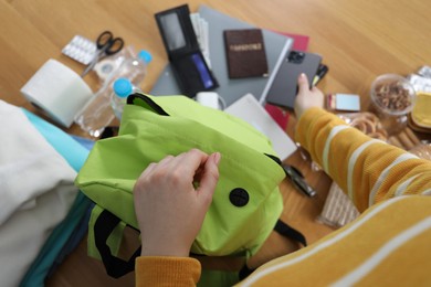 Photo of Survival kit. Woman packing different emergency supplies into backpack at wooden table indoors, above view