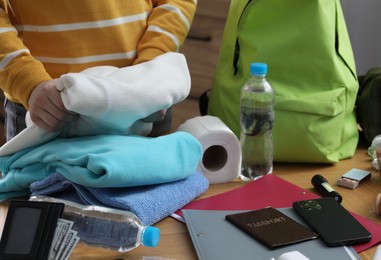 Photo of Survival kit. Woman packing different emergency supplies at wooden table indoors, closeup