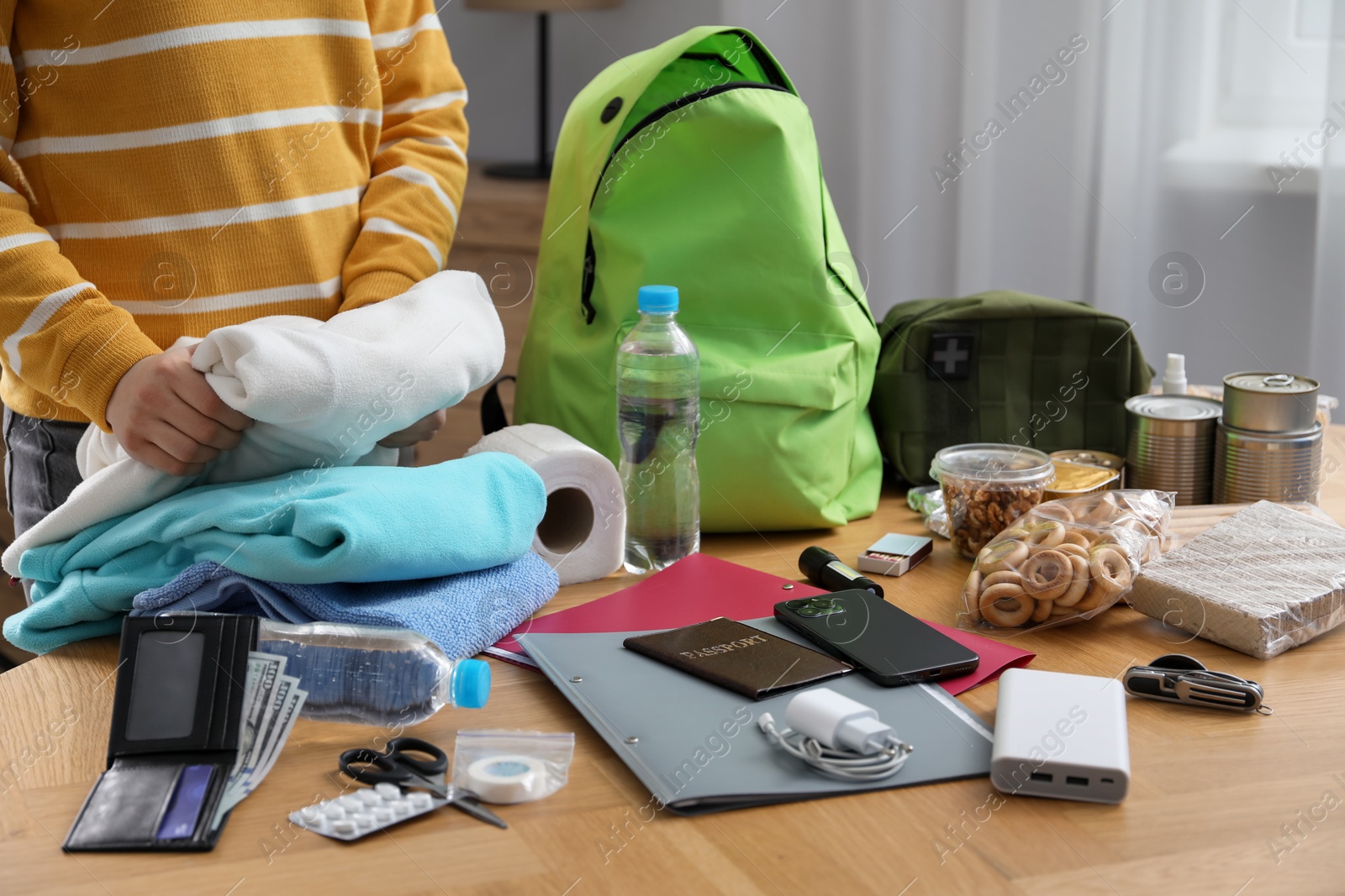 Survival kit. Woman packing different emergency supplies at wooden table indoors, closeup Photo of Survival kit. Woman packing different emergency supplies at wooden table indoors, closeup