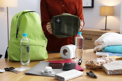 Photo of Survival kit. Woman packing different emergency supplies at wooden table indoors, closeup