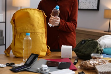 Photo of Survival kit. Woman packing different emergency supplies at wooden table indoors, closeup