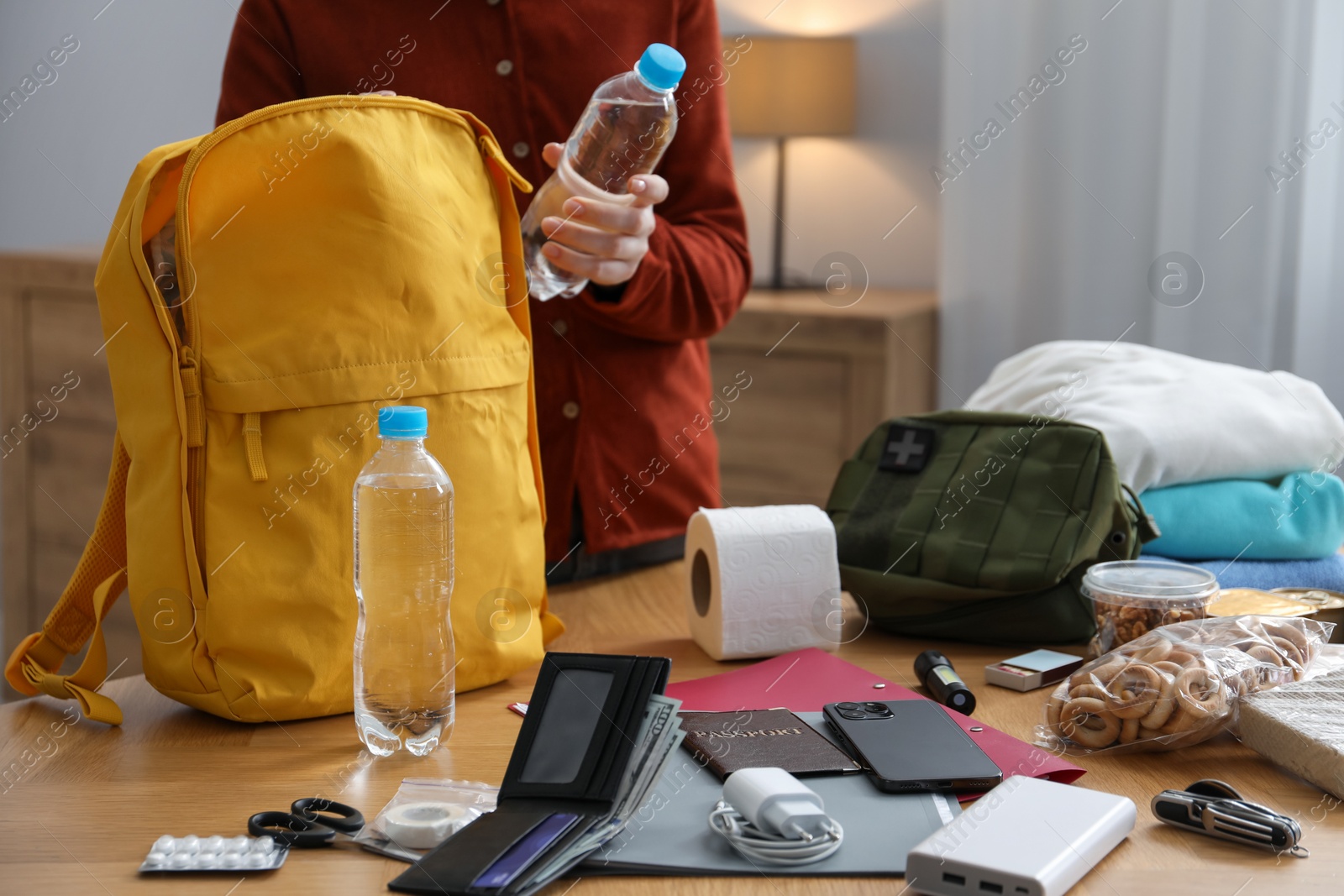 Survival kit. Woman packing different emergency supplies into backpack at wooden table indoors, closeup Photo of Survival kit. Woman packing different emergency supplies into backpack at wooden table indoors, closeup