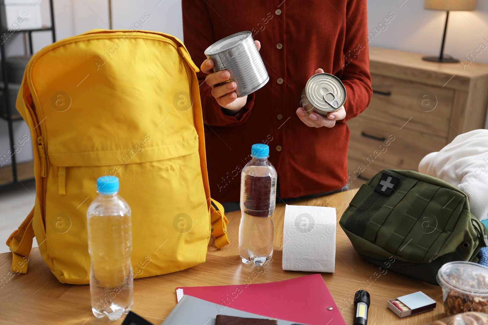 Survival kit. Woman packing different emergency supplies into backpack at wooden table indoors, closeup Photo of Survival kit. Woman packing different emergency supplies into backpack at wooden table indoors, closeup