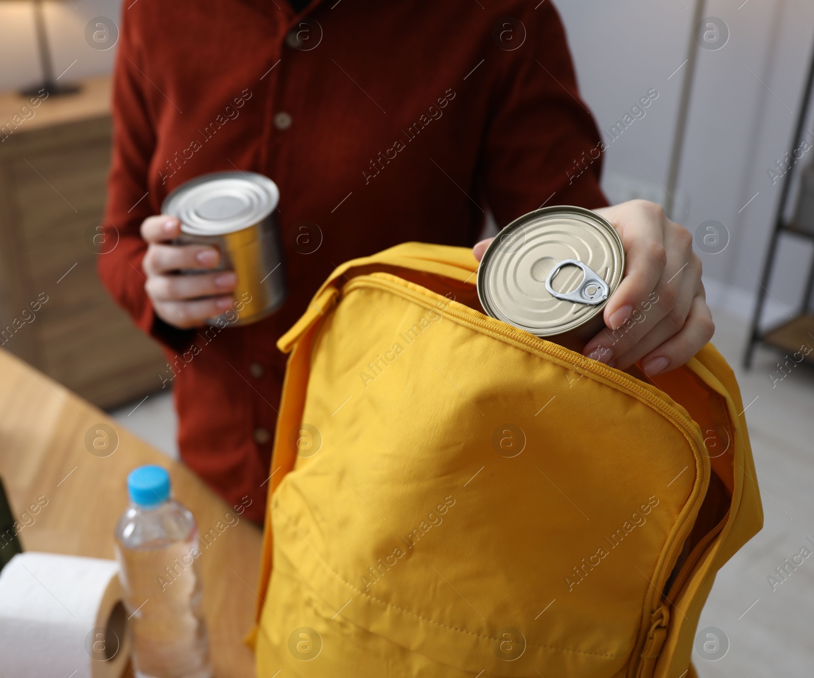 Survival kit. Woman packing different emergency supplies into backpack at table indoors, closeup Photo of Survival kit. Woman packing different emergency supplies into backpack at table indoors, closeup