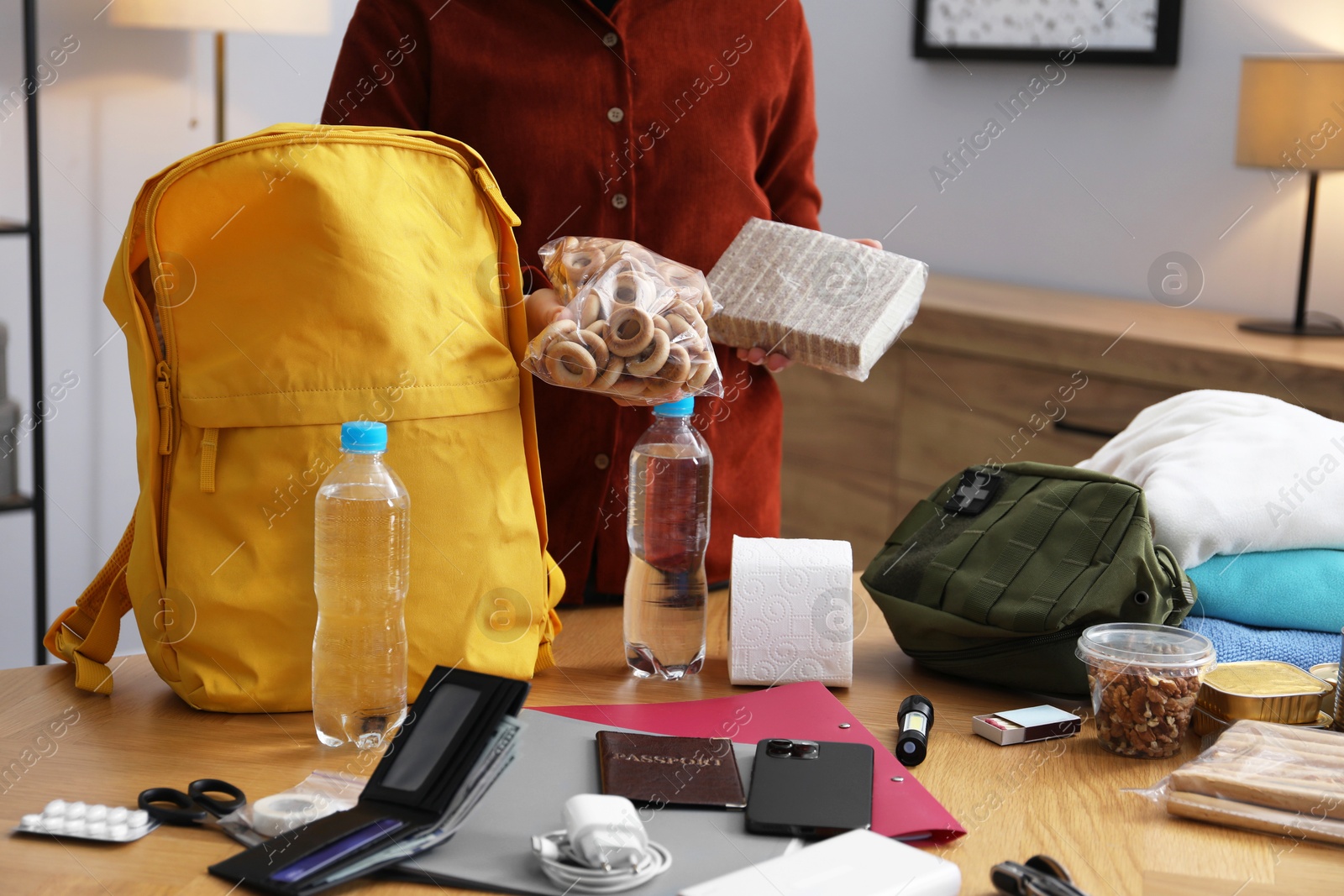 Survival kit. Woman packing different emergency supplies into backpack at wooden table indoors, closeup Photo of Survival kit. Woman packing different emergency supplies into backpack at wooden table indoors, closeup
