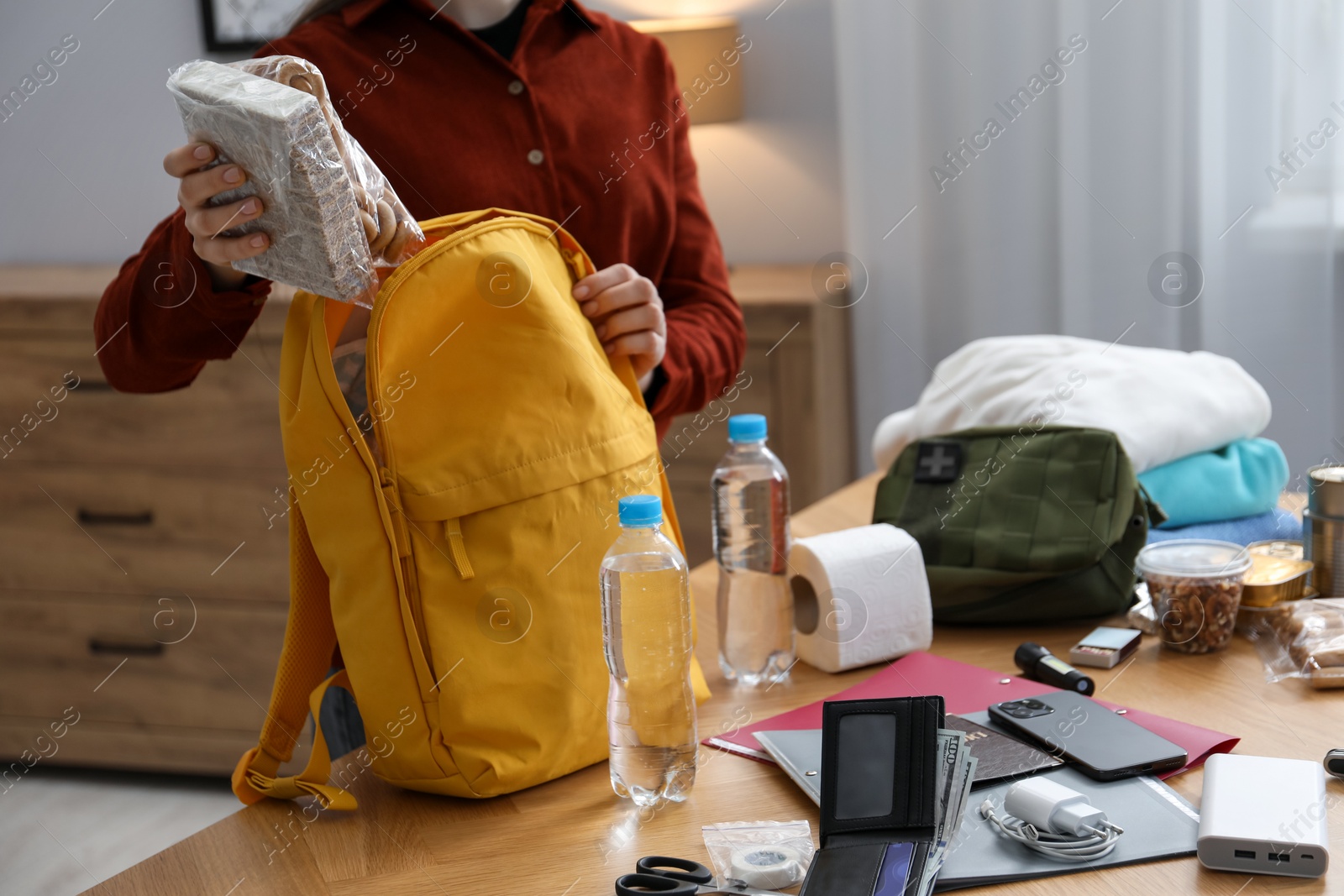Survival kit. Woman packing different emergency supplies into backpack at wooden table indoors, closeup Photo of Survival kit. Woman packing different emergency supplies into backpack at wooden table indoors, closeup