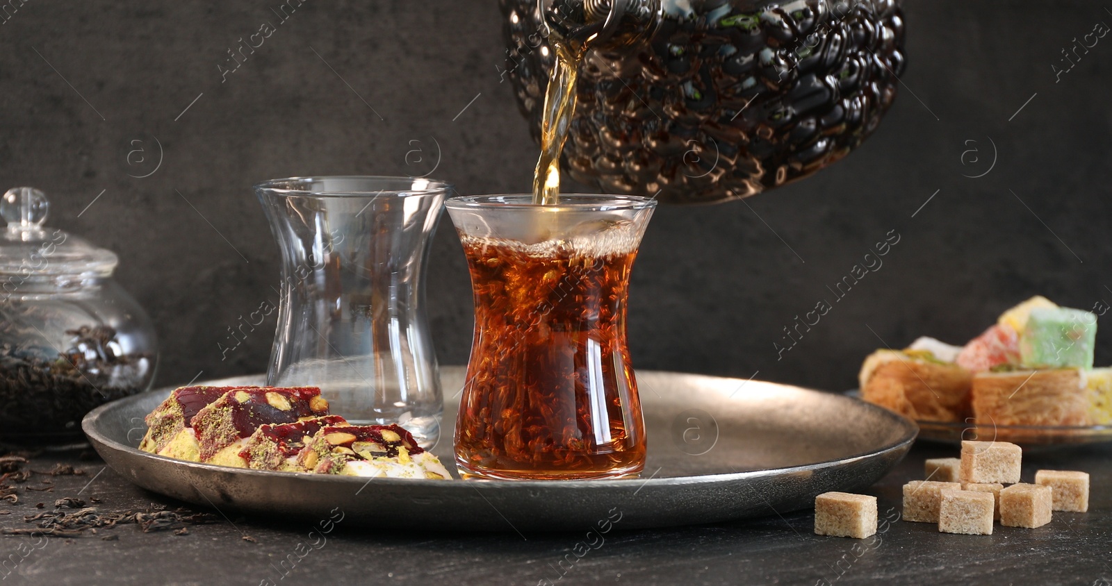 Pouring hot Turkish tea into glass cup at black table, closeup Photo of Pouring hot Turkish tea into glass cup at black table, closeup