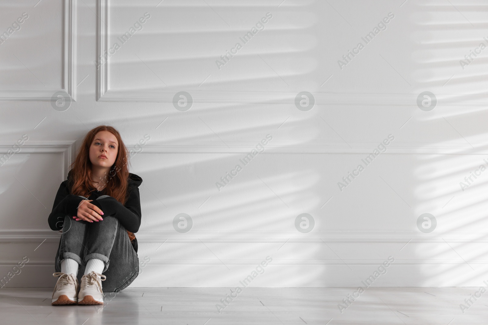 Sad teenage girl sitting on floor near light wall indoors, space for text Photo of Sad teenage girl sitting on floor near light wall indoors, space for text