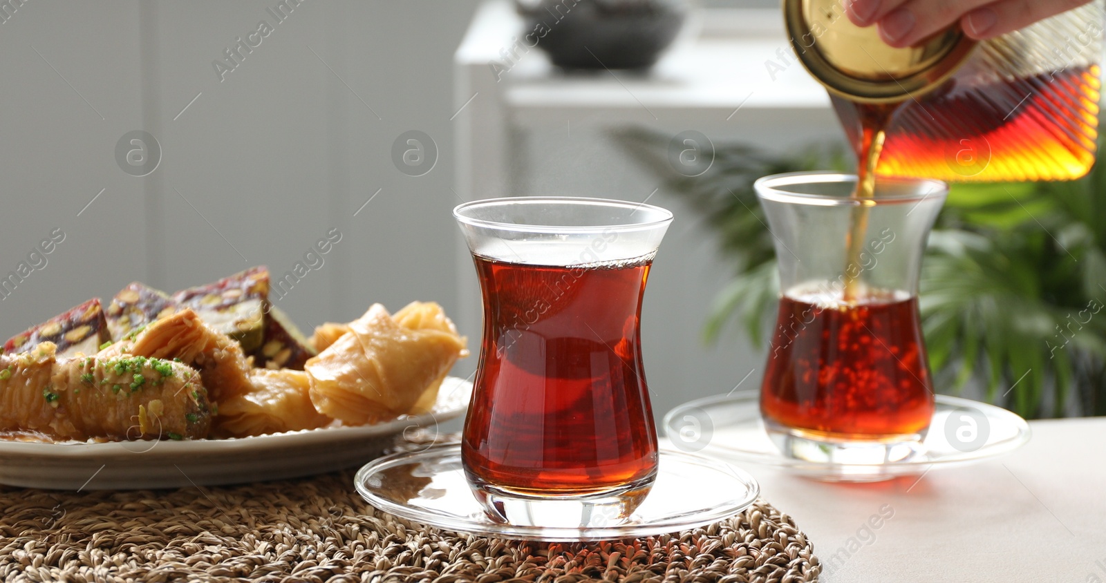 Woman pouring Turkish tea into glass cup at table indoors, selective focus Photo of Woman pouring Turkish tea into glass cup at table indoors, selective focus