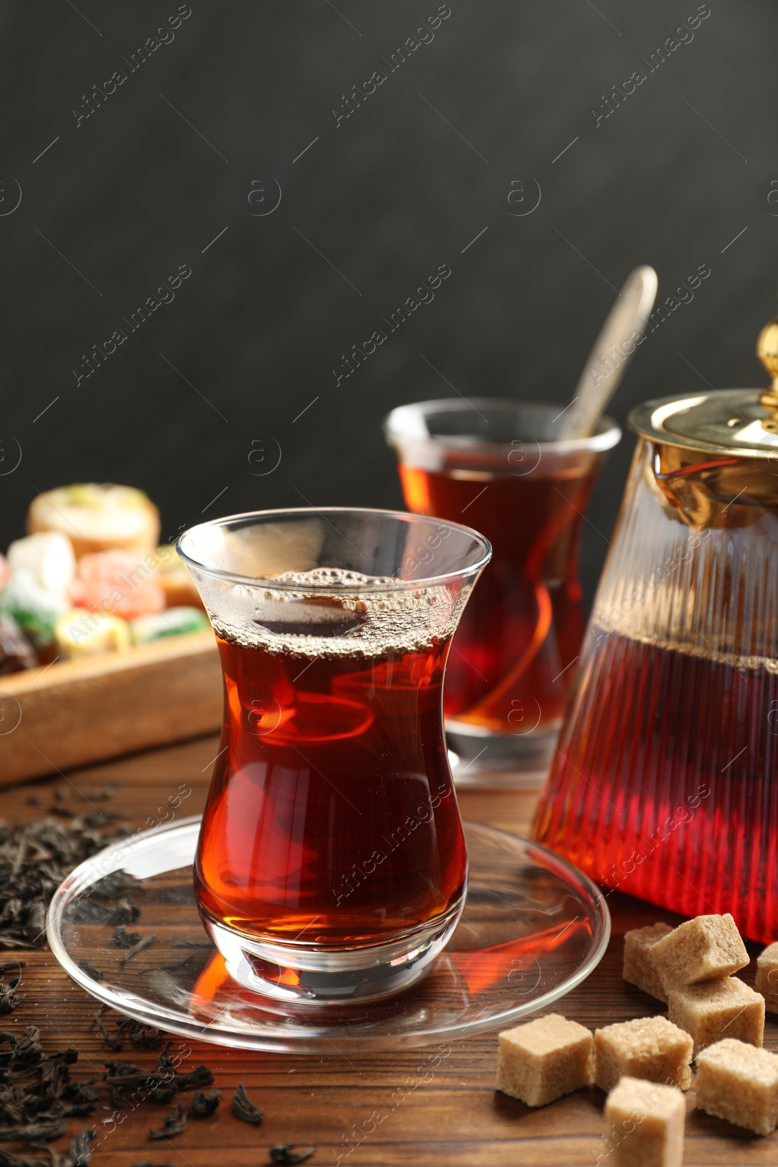 Traditional Turkish tea in glass cups, teapot, dry leaves, brown sugar and sweets on wooden table, closeup Photo of Traditional Turkish tea in glass cups, teapot, dry leaves, brown sugar and sweets on wooden table, closeup