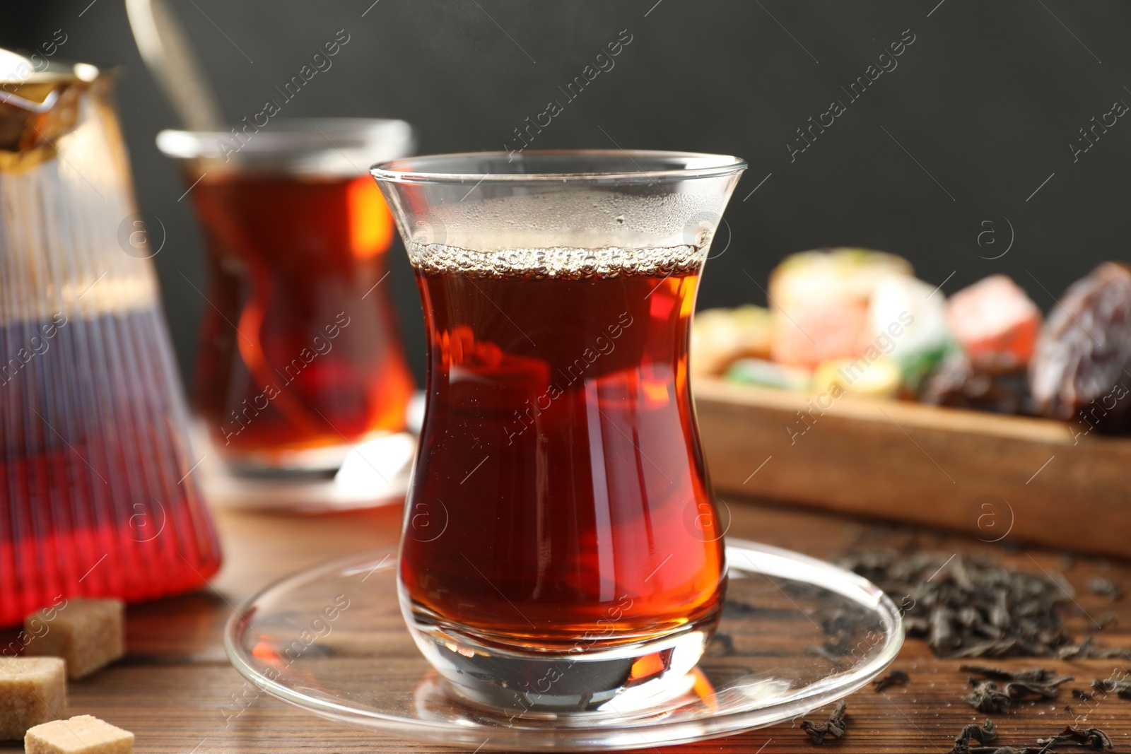 Traditional Turkish tea in glass cups, teapot, dry leaves, brown sugar and sweets on wooden table, closeup Photo of Traditional Turkish tea in glass cups, teapot, dry leaves, brown sugar and sweets on wooden table, closeup
