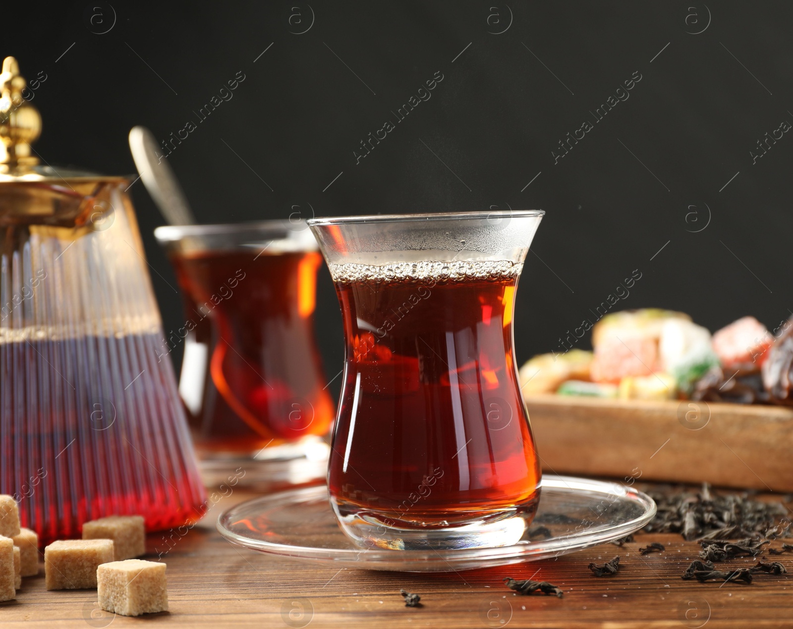 Traditional Turkish tea in glass cups, teapot, dry leaves, brown sugar and sweets on wooden table, closeup Photo of Traditional Turkish tea in glass cups, teapot, dry leaves, brown sugar and sweets on wooden table, closeup