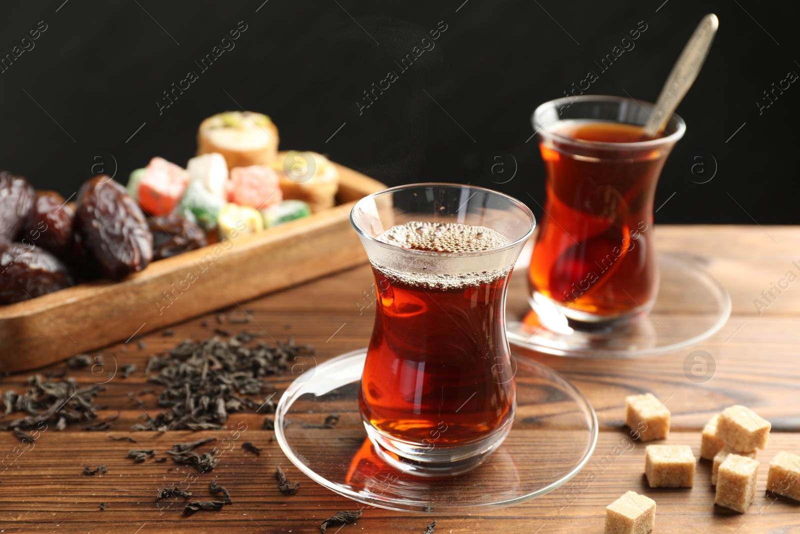 Traditional Turkish tea in glass cups, dry leaves, brown sugar and sweets on wooden table, closeup Photo of Traditional Turkish tea in glass cups, dry leaves, brown sugar and sweets on wooden table, closeup