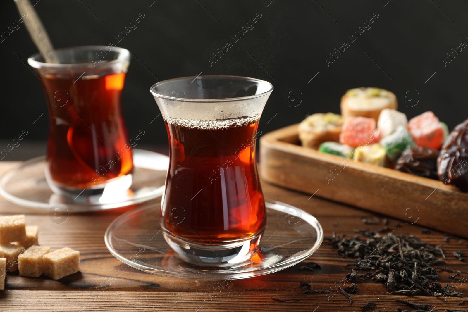 Traditional Turkish tea in glass cups, dry leaves, brown sugar and sweets on wooden table, closeup Photo of Traditional Turkish tea in glass cups, dry leaves, brown sugar and sweets on wooden table, closeup