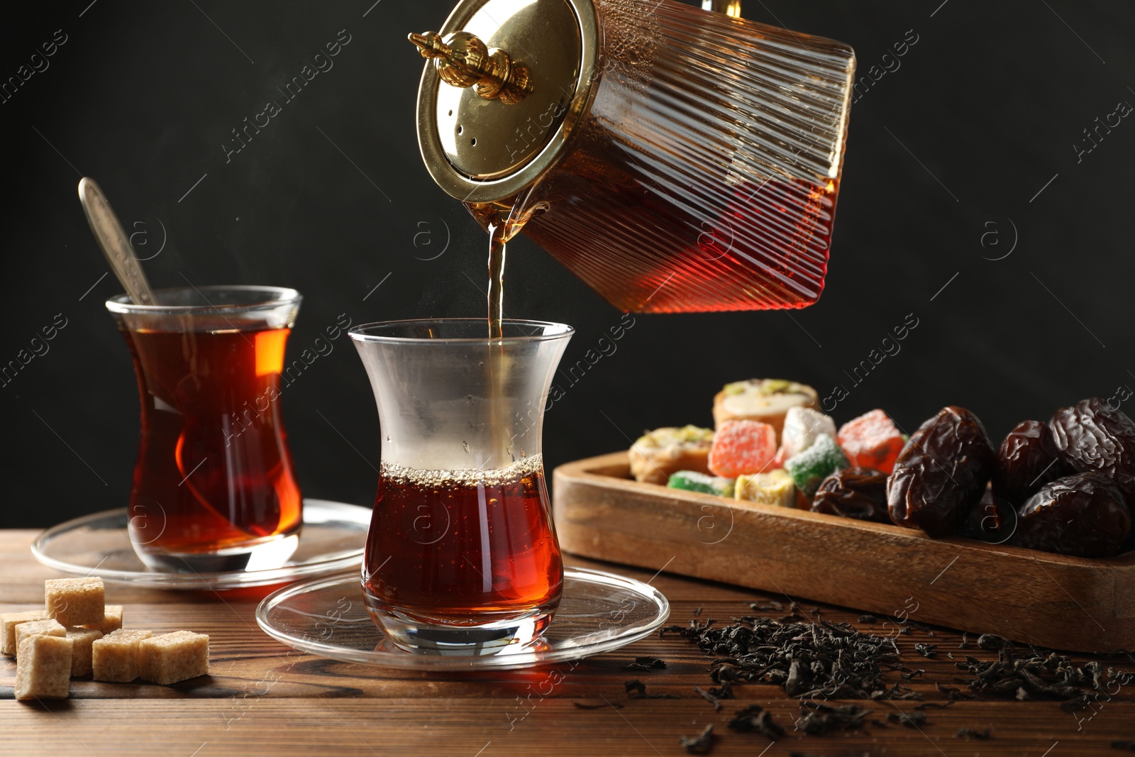 Pouring Turkish tea into glass cup at wooden table, closeup Photo of Pouring Turkish tea into glass cup at wooden table, closeup