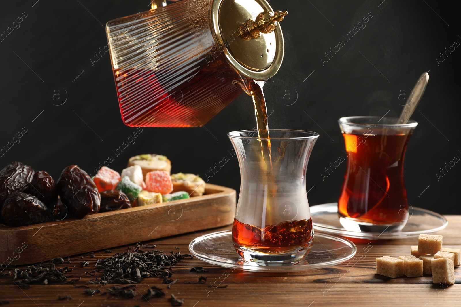 Pouring Turkish tea into glass cup at wooden table, closeup Photo of Pouring Turkish tea into glass cup at wooden table, closeup