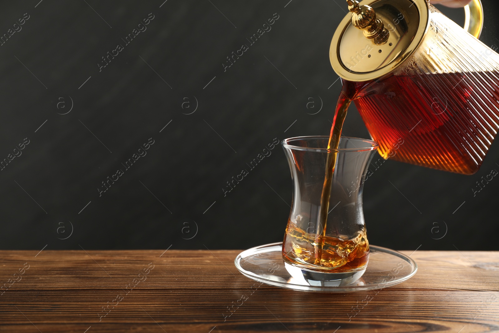 Pouring Turkish tea into glass cup at wooden table, closeup. Space for text Photo of Pouring Turkish tea into glass cup at wooden table, closeup. Space for text