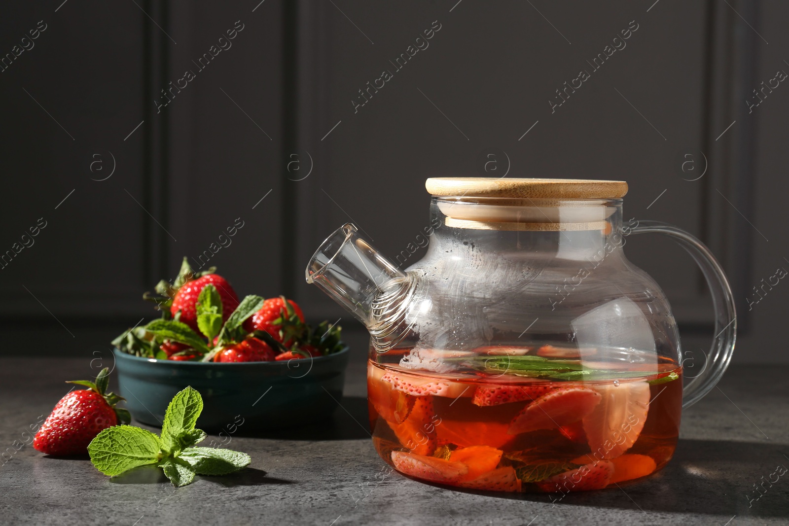 Glass teapot with aromatic fruit tea, strawberries and mint on grey table Photo of Glass teapot with aromatic fruit tea, strawberries and mint on grey table