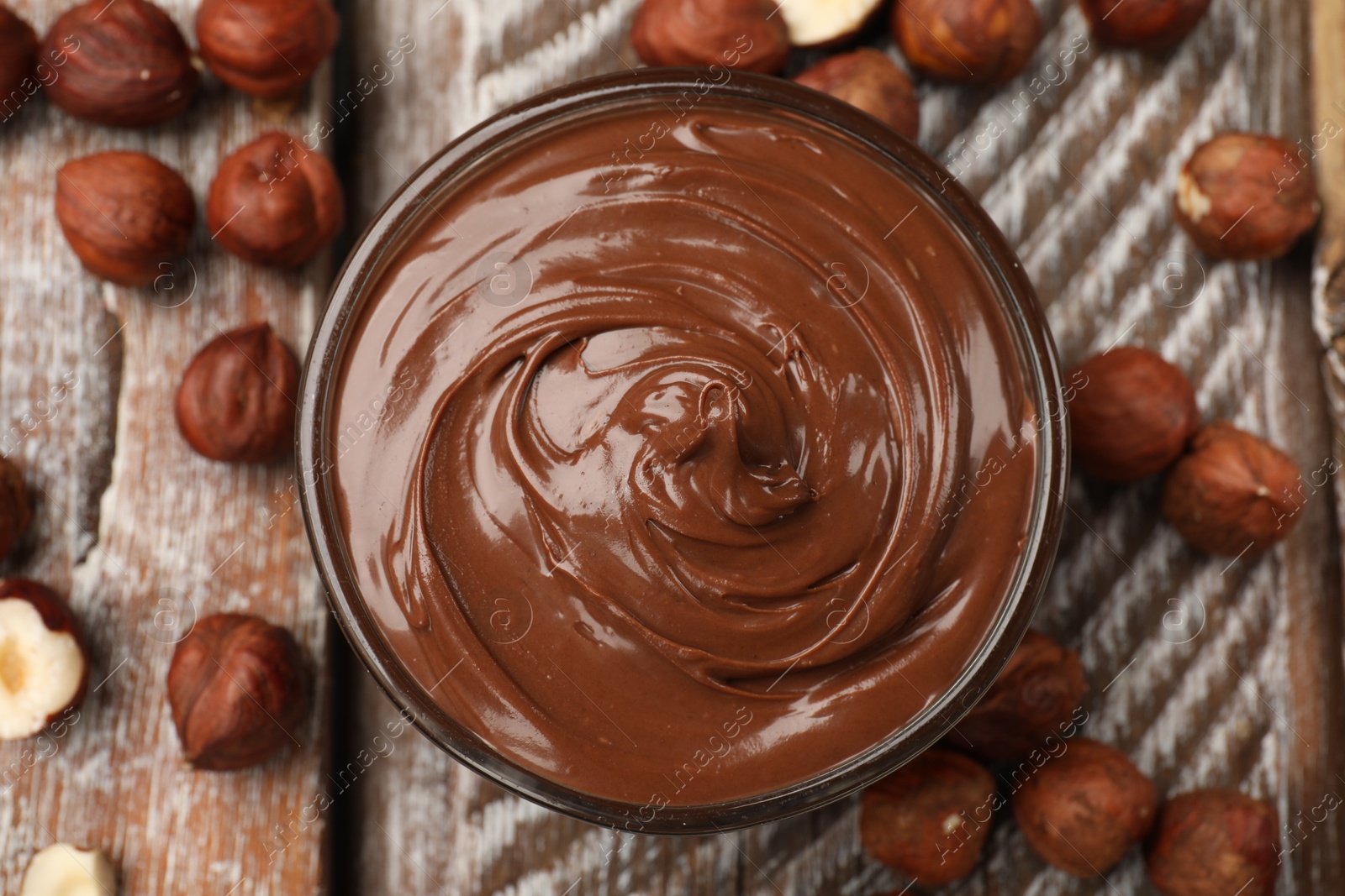 Chocolate hazelnut spread in bowl and nuts on wooden table, flat lay Photo of Chocolate hazelnut spread in bowl and nuts on wooden table, flat lay