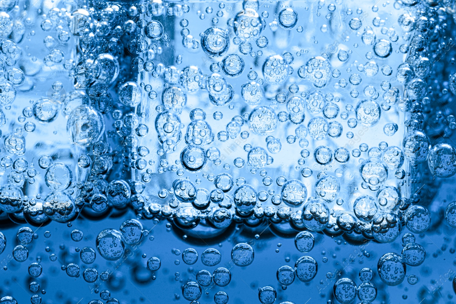 Soda water with bubbles and ice cubes as background, closeup Image of Soda water with bubbles and ice cubes as background, closeup