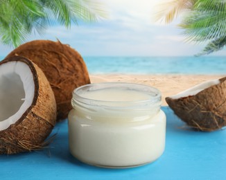 Image of Cooking oil in jar and coconuts on blue table against beach
