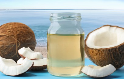 Image of Cooking oil in jar and coconuts on blue table against beach