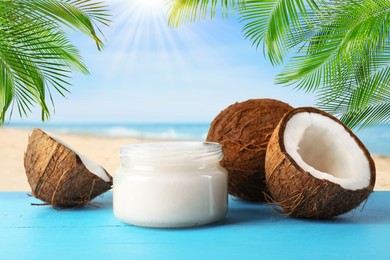 Image of Cooking oil in jar and coconuts on blue table against beach