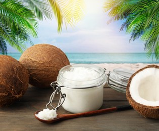 Image of Cooking oil in jar and coconuts on wooden table against beach