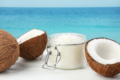 Image of Cooking oil in jar and coconuts on white table against sea