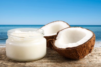 Image of Cooking oil in jar and coconut on wooden table against beach